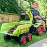 Žalias pedalinis traktorius CLAAS su kaušu, krautuvu ir priekaba