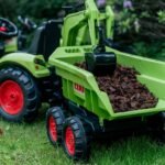 Žalias pedalinis traktorius CLAAS su kaušu, krautuvu ir priekaba