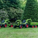 Žalias pedalinis traktorius CLAAS su kaušu, krautuvu ir priekaba